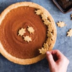 Overhead shot of pumpkin pie on a blue background with maple leaf decorations.