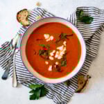 Close up overhead shot of an easy red pepper and tomato soup, topped with goat cheese and garnished with fresh herbs.