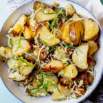 Overhead shot of sliced, roasted Russet potatoes topped with chopped rosemary and parmesan.