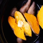 Close up of sliced baked sweet potatoes topped with butter in a black slow cooker.