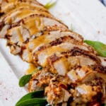 Side shot of sliced turkey breast drizzled with gravy with sage leaves scattered around.