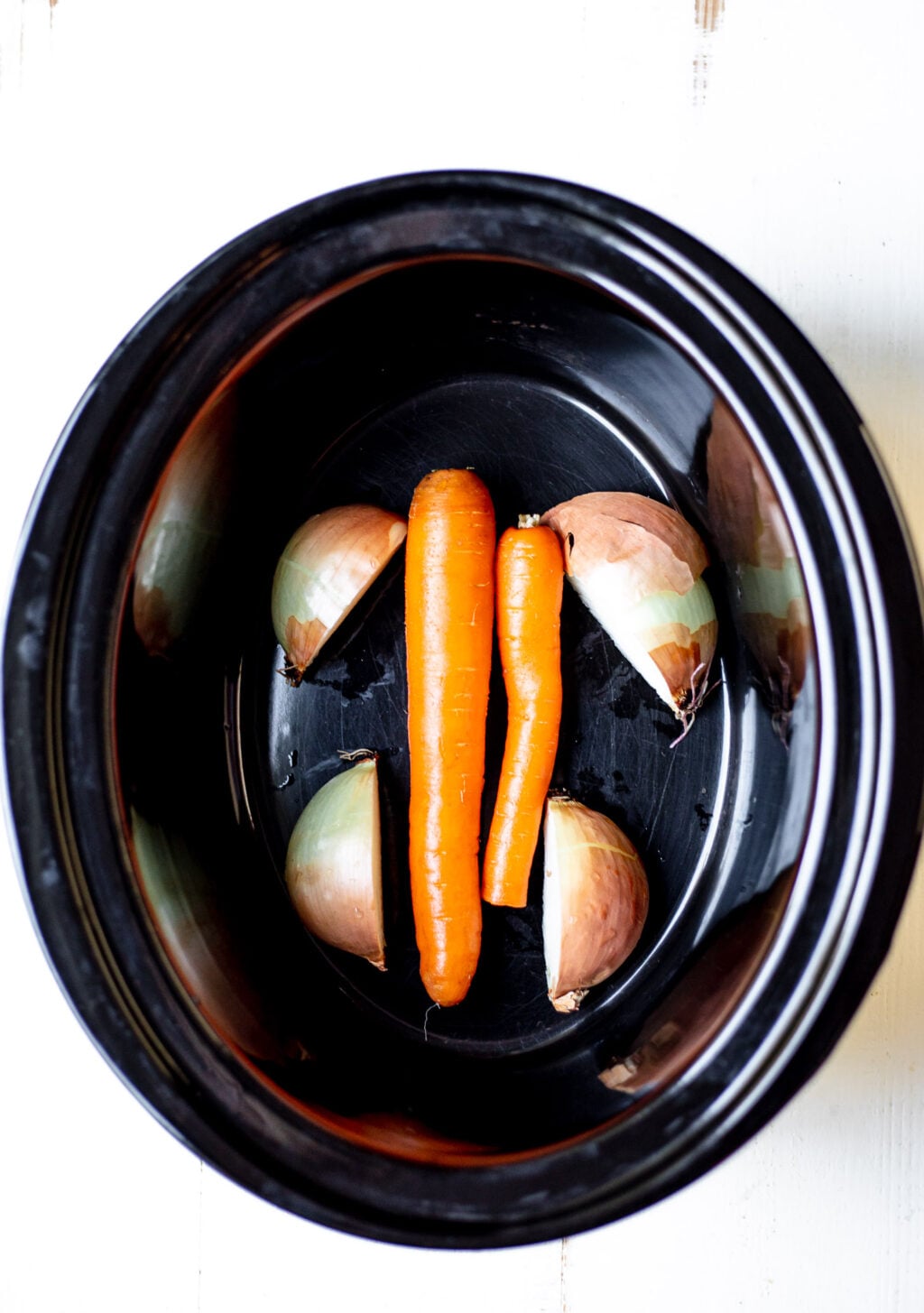 Overhead shot of carrots and onion in a slow cooker.