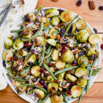 Overhead shot of roasted green beans, Brussels sprouts, pecans, and cranberries on a serving platter.
