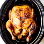 Overhead shot of a cooked whole chicken in a black slow cooker.