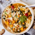 Minestrone soup with butternut squash, beans, and pasta in a bowl on a blue background.