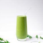 Side shot of a green smoothie in a clear glass with clear straw.