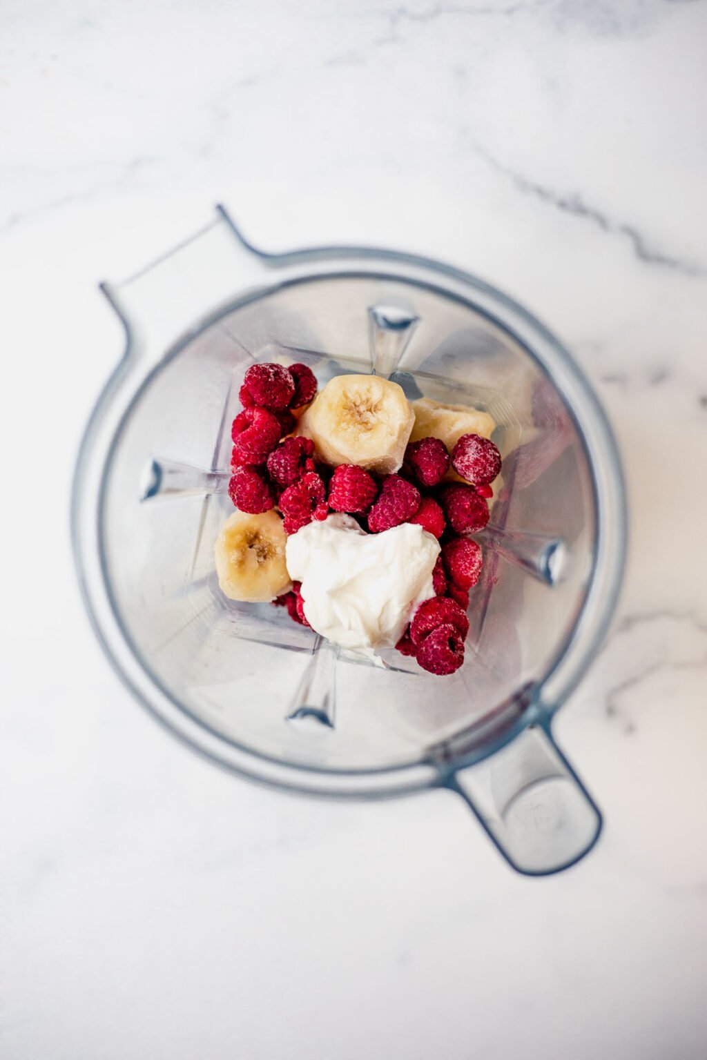 Overhead shot of raspberries, frozen bananas, and yogurt in a blender.