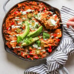 Tortilla strips, chicken, black beans and vegetables topped with cheese, avocado, and sour cream in a skillet.