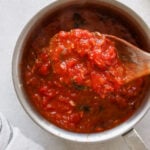 A wooden spoon with a scoop of chunky marinara sauce.