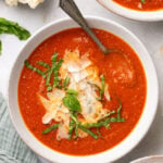 Three bowls of tomato soup topped with basil, parmesan, with crusty bread on the side.