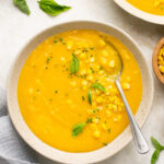Overhead shot of bowls of creamy potato corn chowder with corn kernels and basil leaves. The bowl in the middle has a spoon in it.