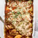 An overhead shot of a white rectangular baking dish filled baked stuffed pasta shells topped with marinara sauce and melted shredded cheese. A silver serving spoon is scooping a shell out of the bottom left corner of the dish.