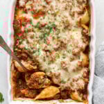 An overhead shot of a white rectangular baking dish filled baked stuffed pasta shells topped with marinara sauce and melted shredded cheese. A silver serving spoon is scooping a shell out of the bottom left corner of the dish.