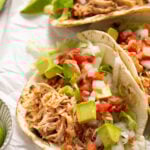 Close up photo of a shredded chicken taco on a small flour tortilla topped with avocado chunks, shredded lettuce, and salsa.