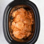Overhead shot of raw chicken tighs covered in an orange sauce in a slow cooker.