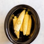 Overhead shot of a slow cooker with corn with a dab of butter.