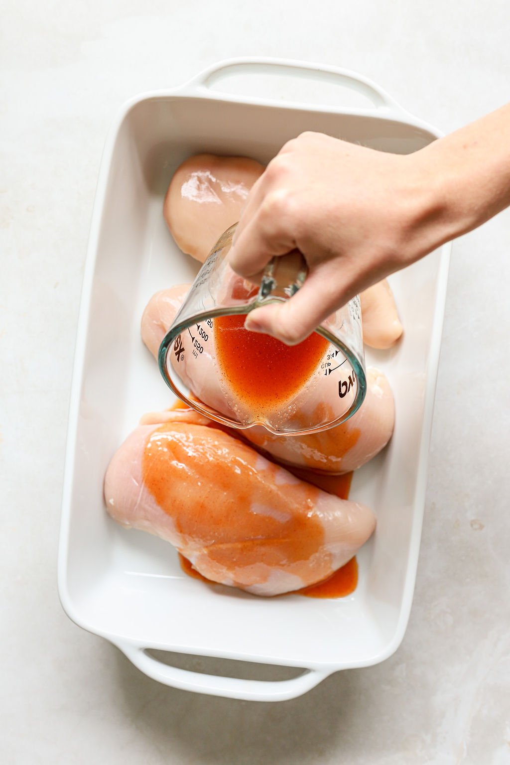 Overhead image of buffalo marinade being poured over raw chicken breast.