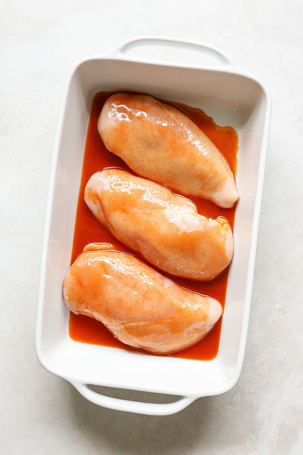 Overhead image of raw chicken breast with buffalo marinade.
