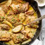 Overhead shot of a serving spoon in a skillet with cooked chicken and apples in a pan sauce.