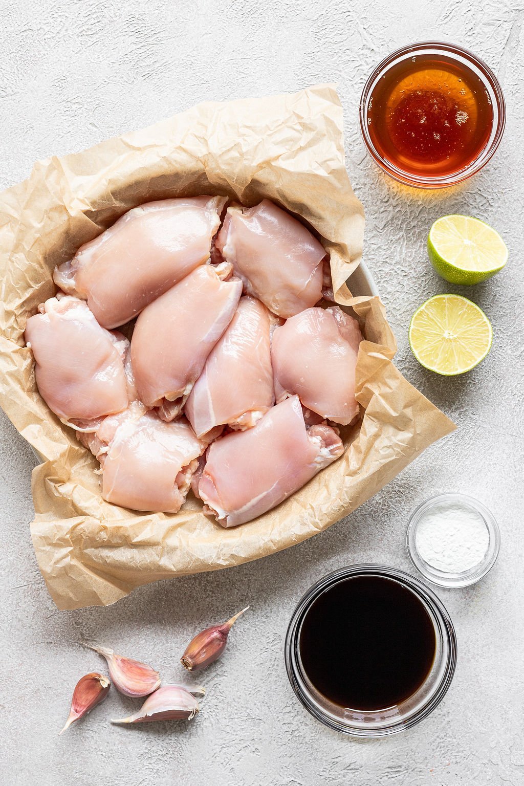 Overhead image of the following ingredients: raw chicken thighs, lime, salt, soy sauce, garlic, and honey.