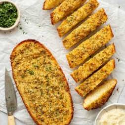 Overhead shot of two halves of a loaf of bread made into garlic bread. One of the halves is sliced.