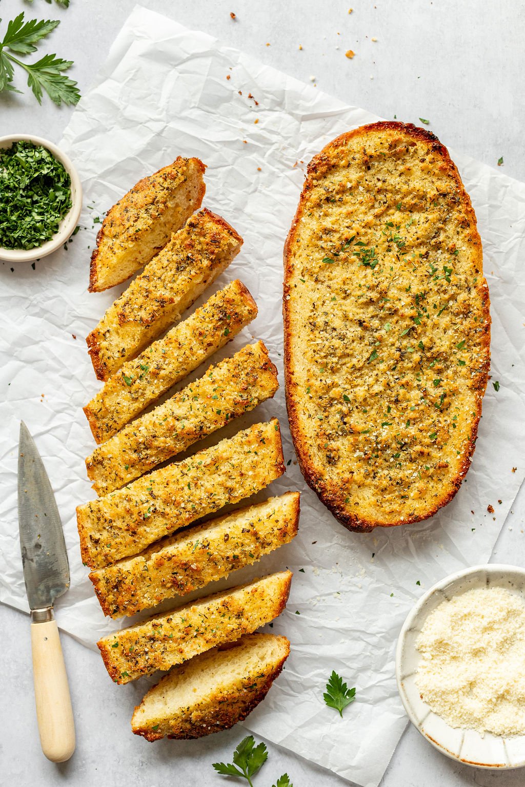Overhead shot of two halves of a loaf of bread made into garlic bread. One of the halves is sliced.