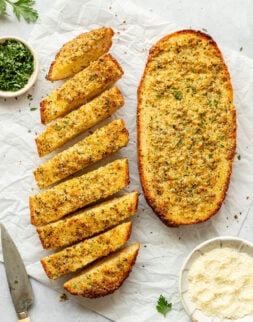 Overhead shot of two halves of a loaf of bread made into garlic bread. One of the halves is sliced.