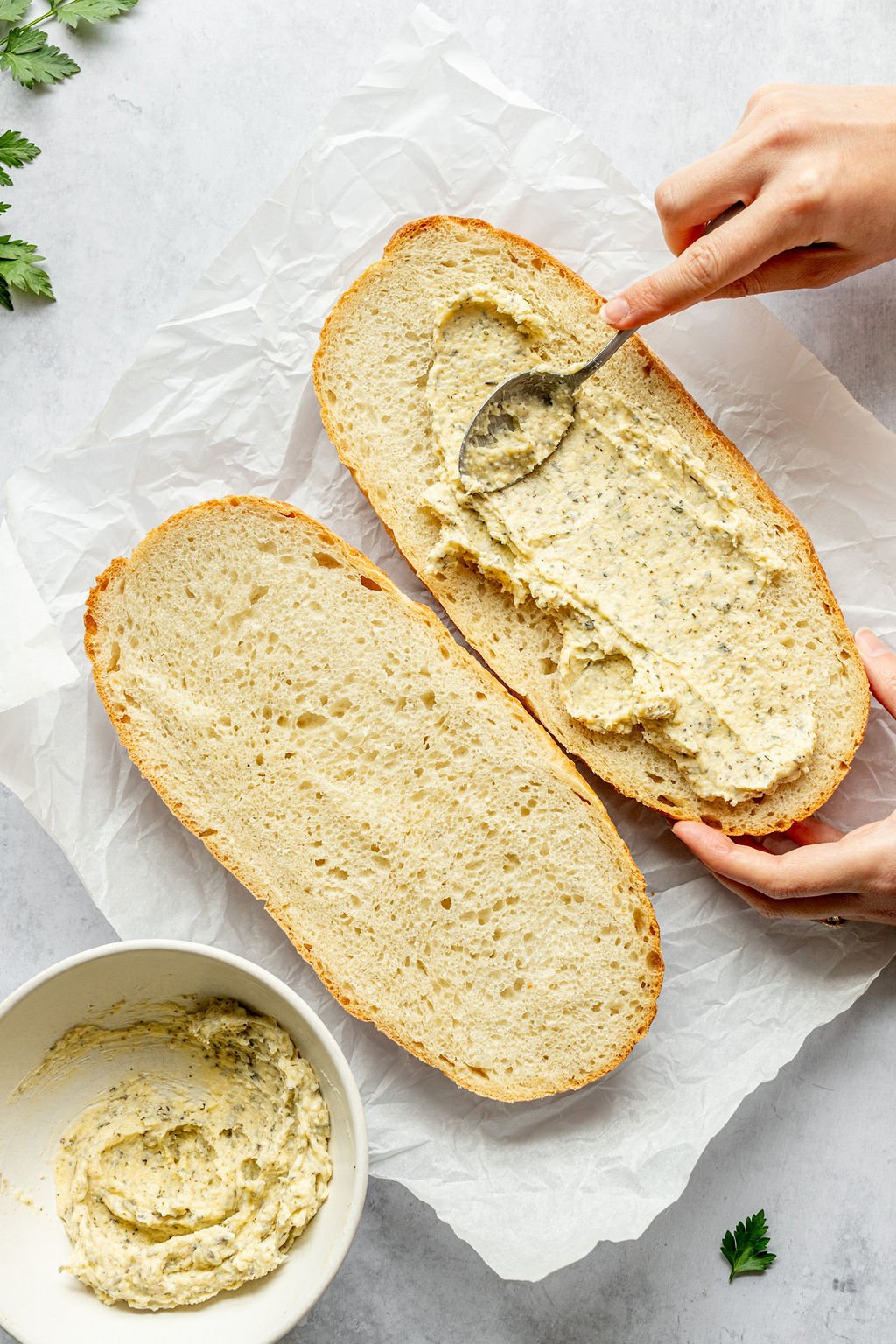 Two halves of a loaf of bread. One is being slathered with a butter mixture.