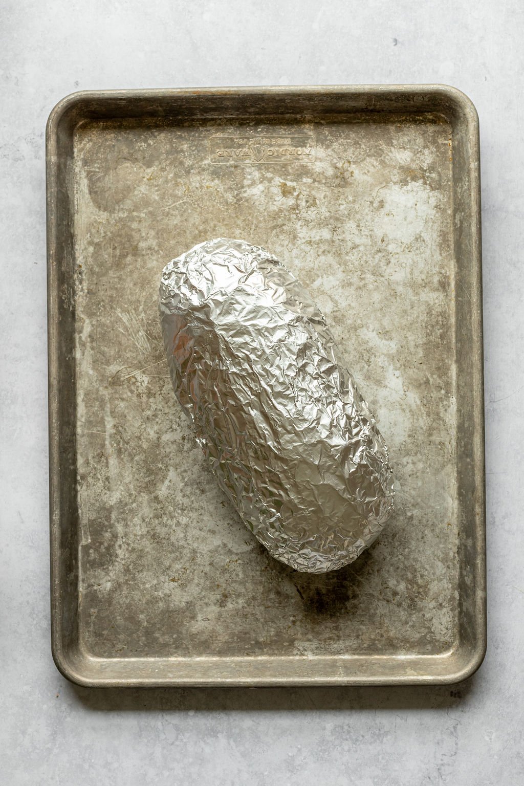 Overhead shot of a baking pan with a loaf of bread covered in aluminum foil.