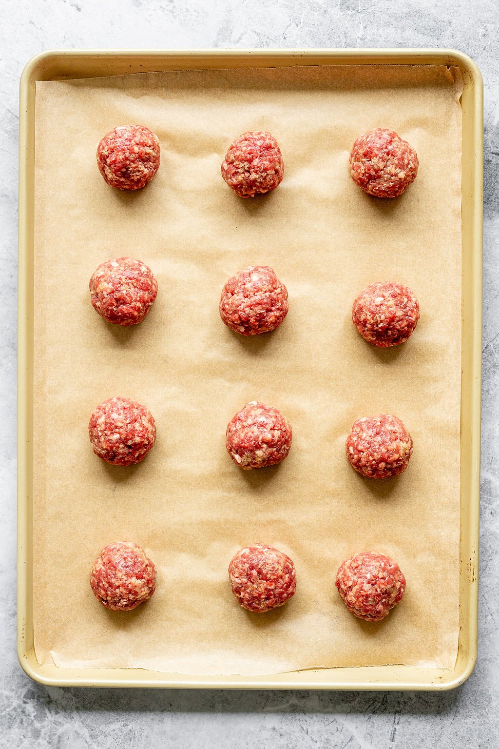 Overhead shot of a parchment lined baking sheet with raw meatballs in a 3 by 4 grid.
