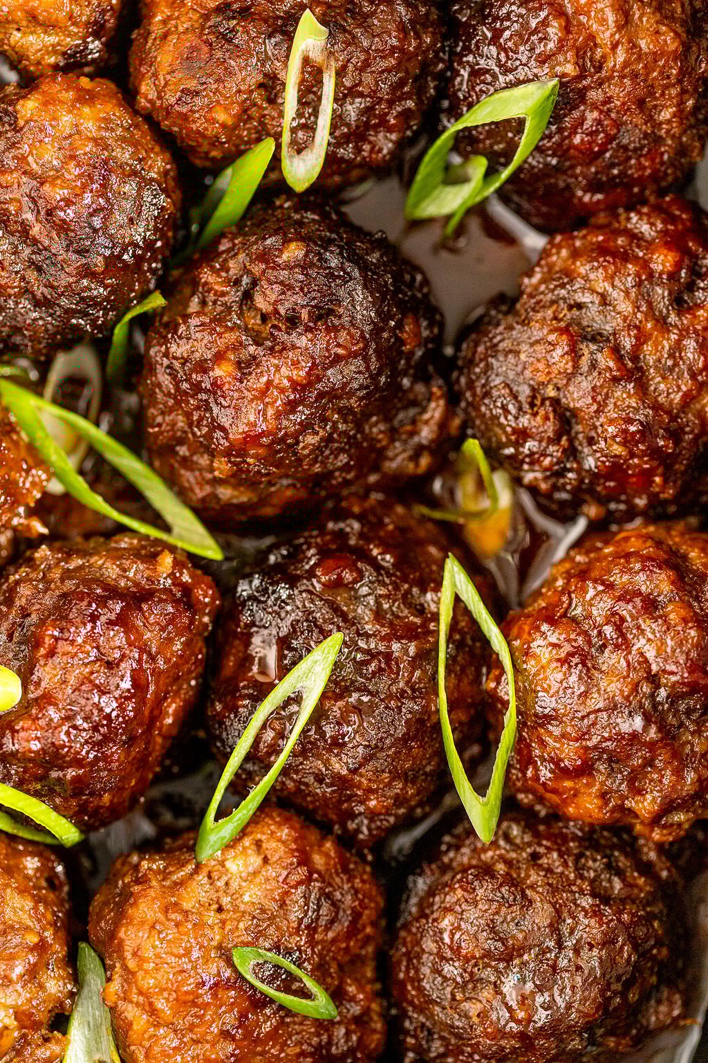 Super zoomed in shot of a pile of meatballs topped with sliced green onions.