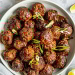 Overhead shot of a white round dish with a pile of meatballs topped with sliced green onions.
