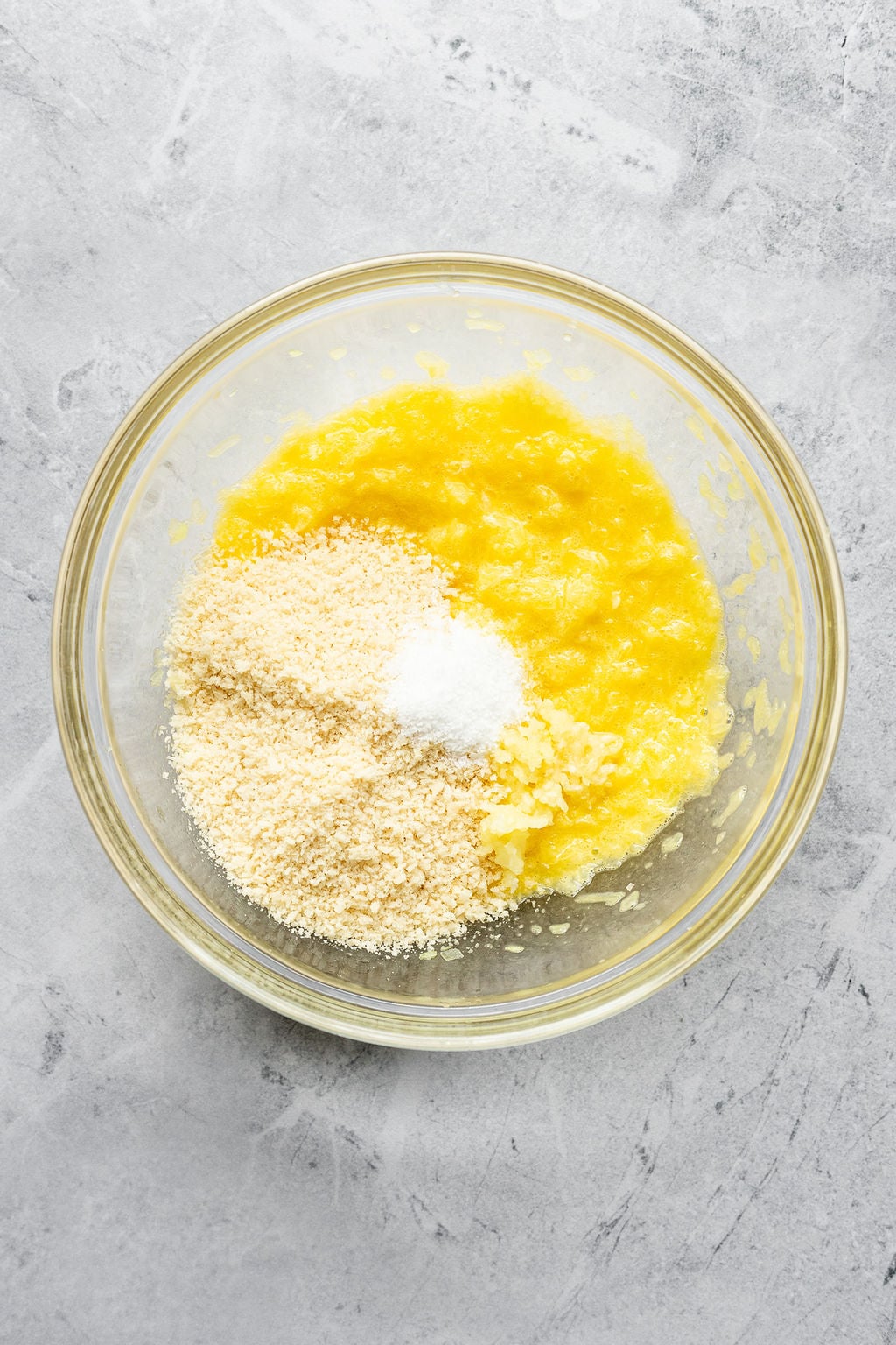 Overhead shot of a glass bowl with egg and grated onion mixture to which breadcrumbs and salt have been added.