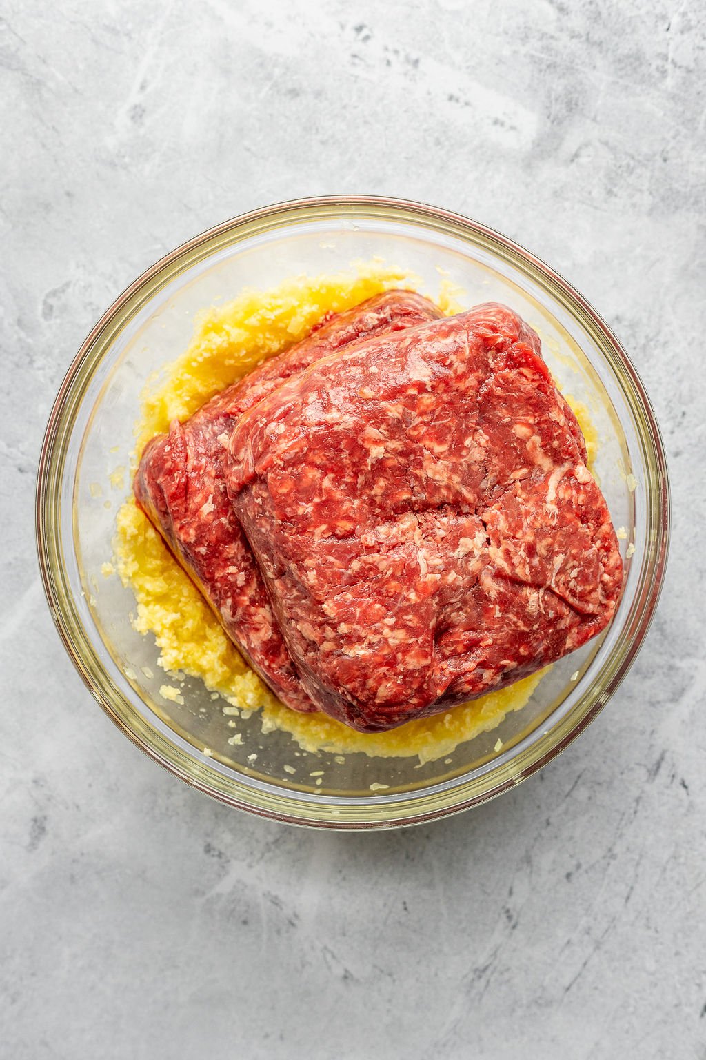 Overhead shot of a glass bowl with raw ground beef on top of a bread crumb mixture.