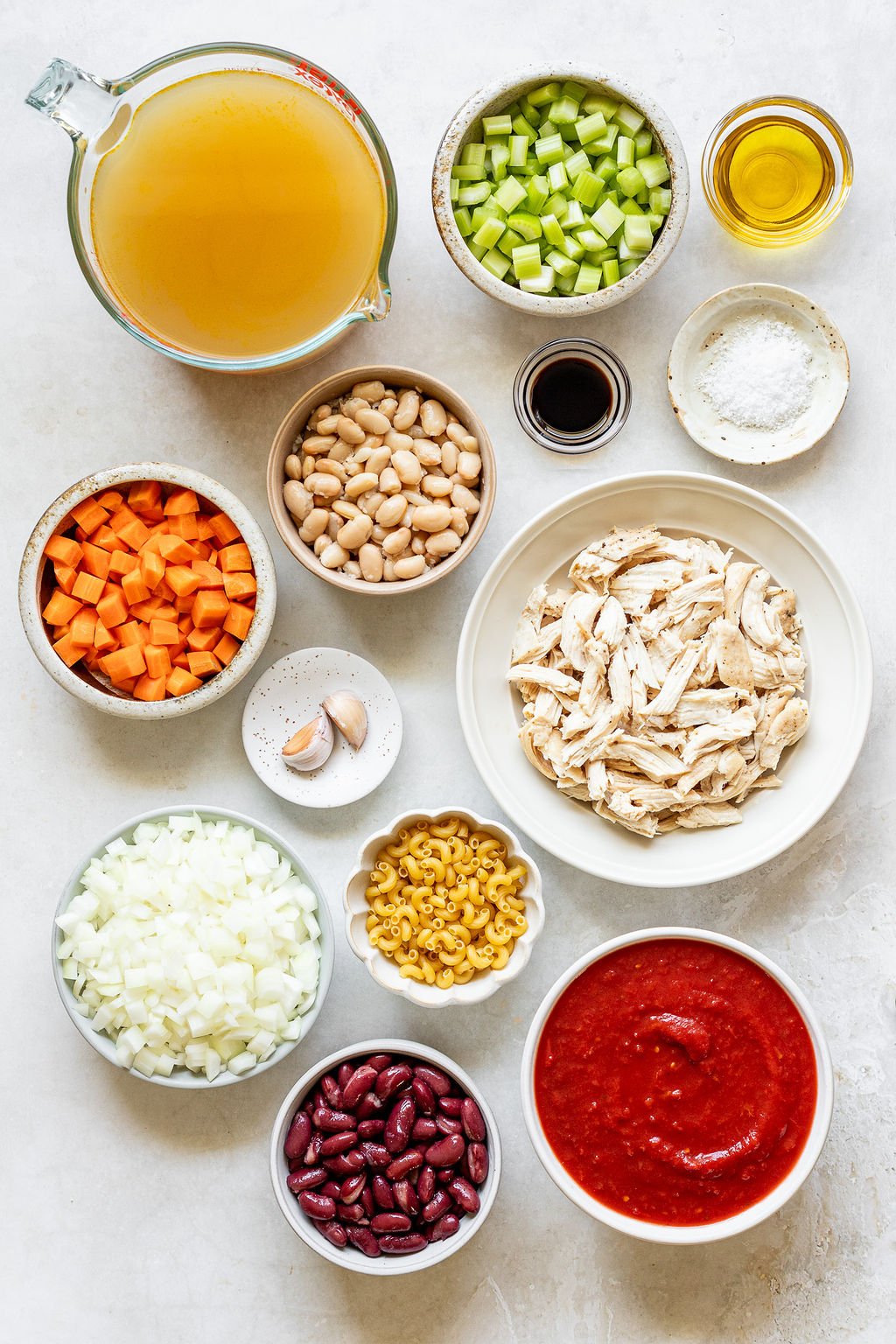 Overhead shot of the following ingredients: broth, beans, celery, carrots, oil, salt, garlic, elbow pasta, tomato sauce, diced onion, and shredded chicken.