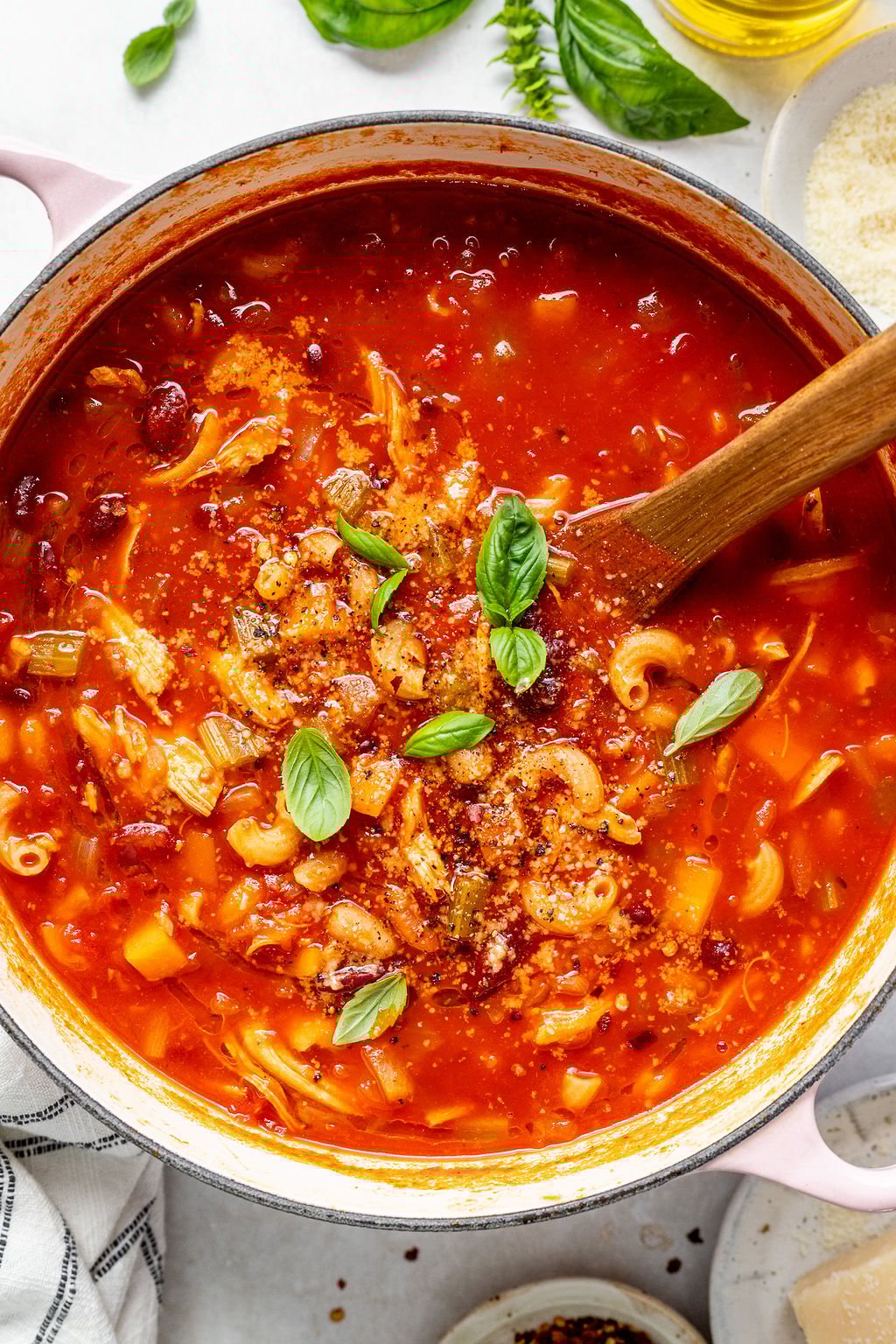 Overhead shot of a pot with a red based soup topped with basil leaves.