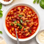 Overhead image of a white bowl with a rad based soup with a spoon in it.
