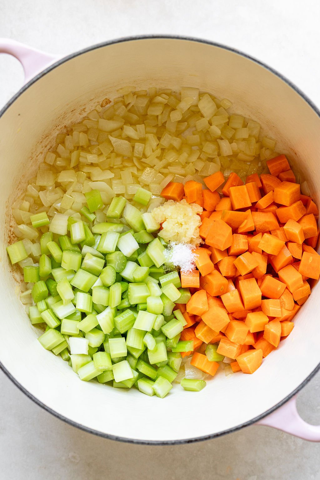 Overhead shot of a pot with cooked onions and added garlic, salt, celery, and carrots.