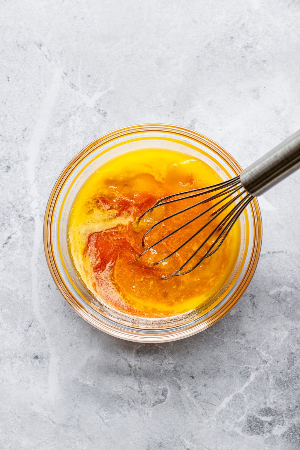 Overhead shot of a small glass bowl with the ingredients for buffalo sauce and a whisk.
