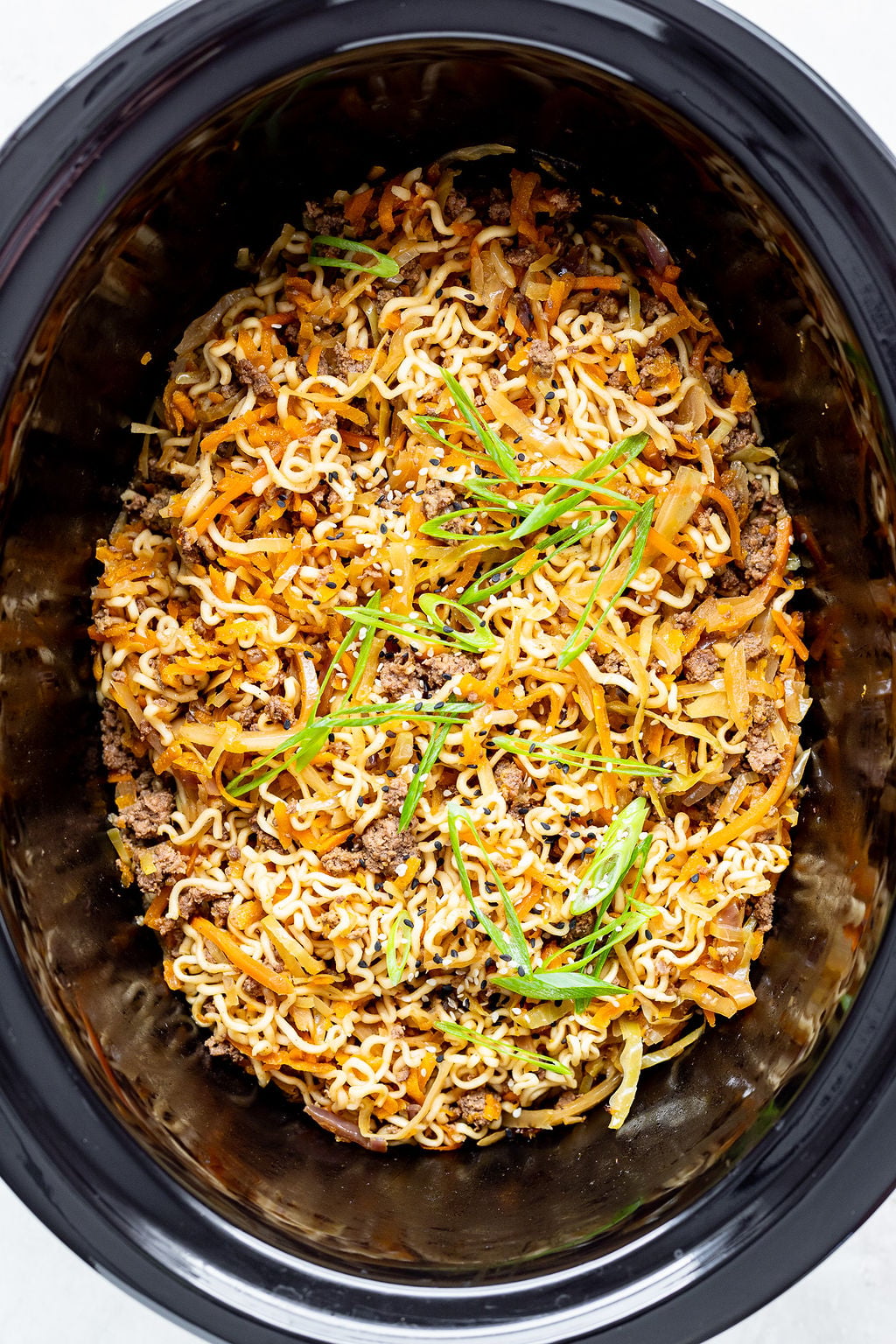 Overhead shot of ramen noodles in a slow cooker topped with sliced green onions and sesame seeds.