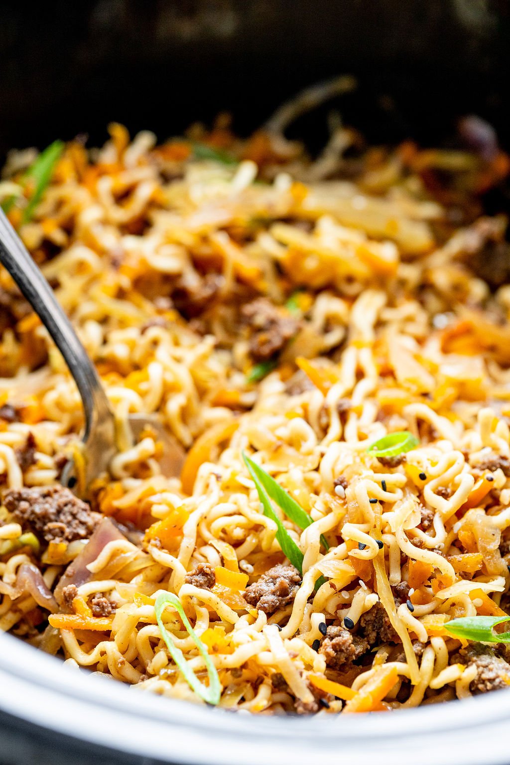 Closeup shot of ramen noodles in a slow cooker. There are chunks of ground beef and slices of green onion in the noodles.
