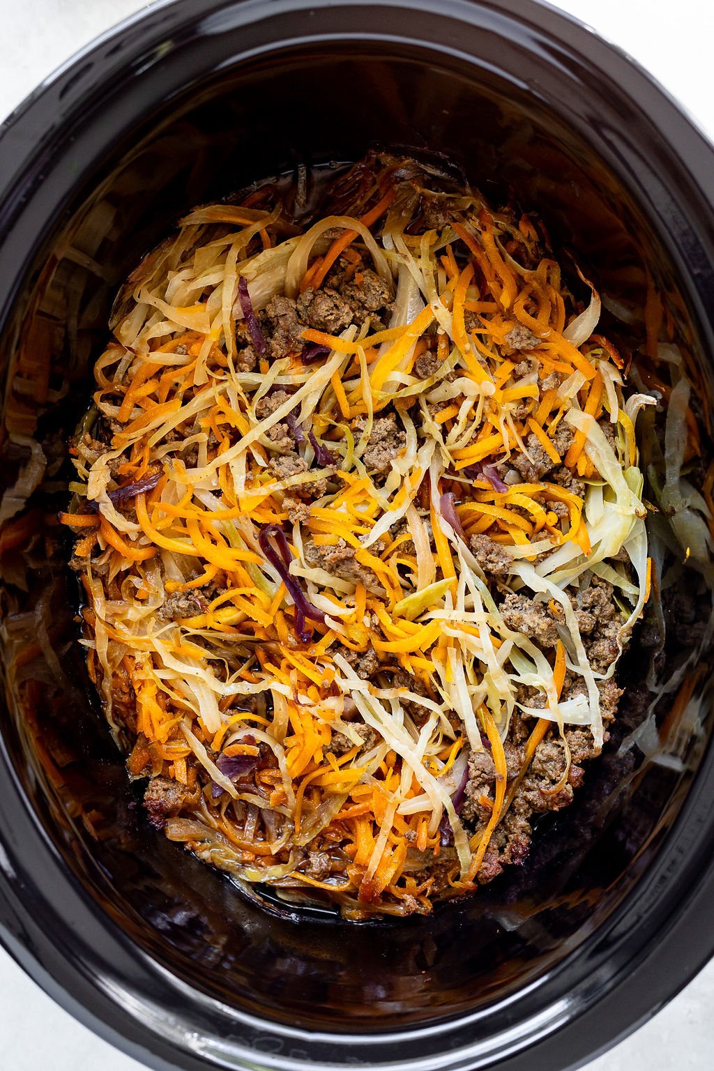 Overhead shot of a slow cooker with cooked ground beef and thinly sliced cabbage and carrots.