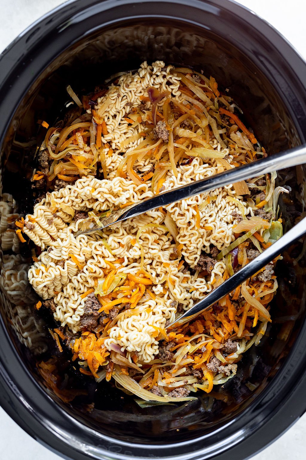 Ramen noodles being stirred into cooked ground beef and thinly sliced cabbage and carrots.
