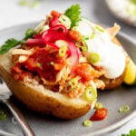 Close up image of grey plate with a fork and a baked potato stuffed with shredded chicken, salsa, scallions, sour cream, and cilantro.