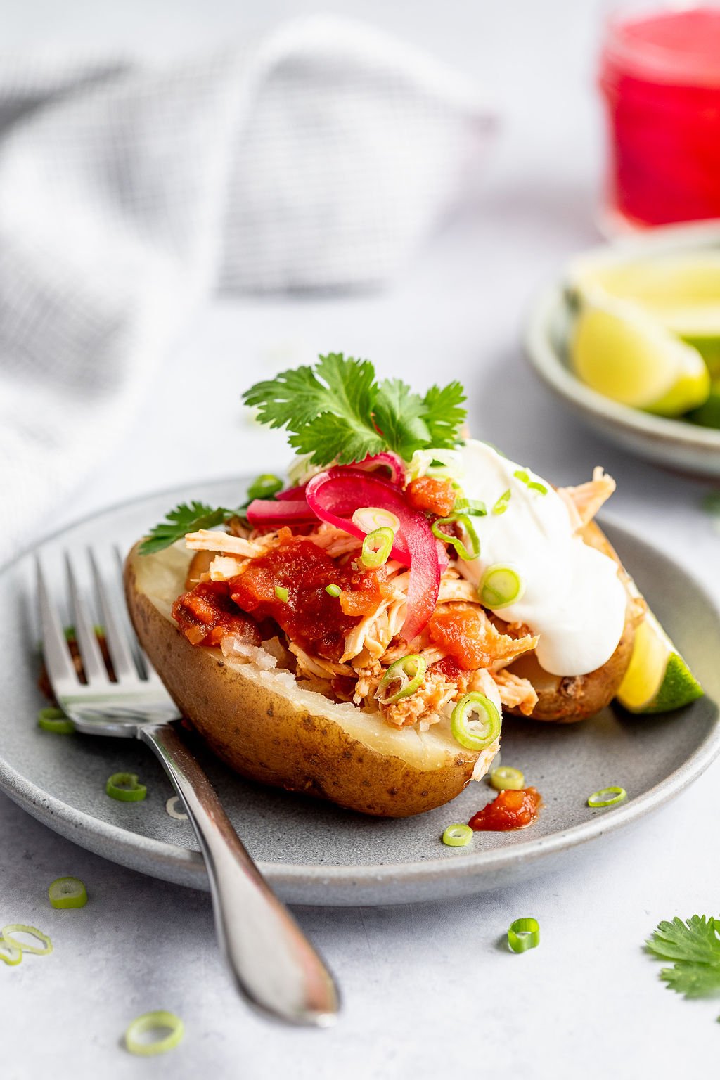Close-up side angle image of grey plate with a fork and a baked potato stuffed with shredded chicken, salsa, scallions, sour cream, and cilantro.