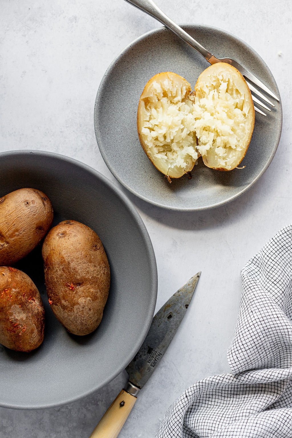 Overhead shot of grey bowl with baked potatoes and a grey plate with an open baked potato.