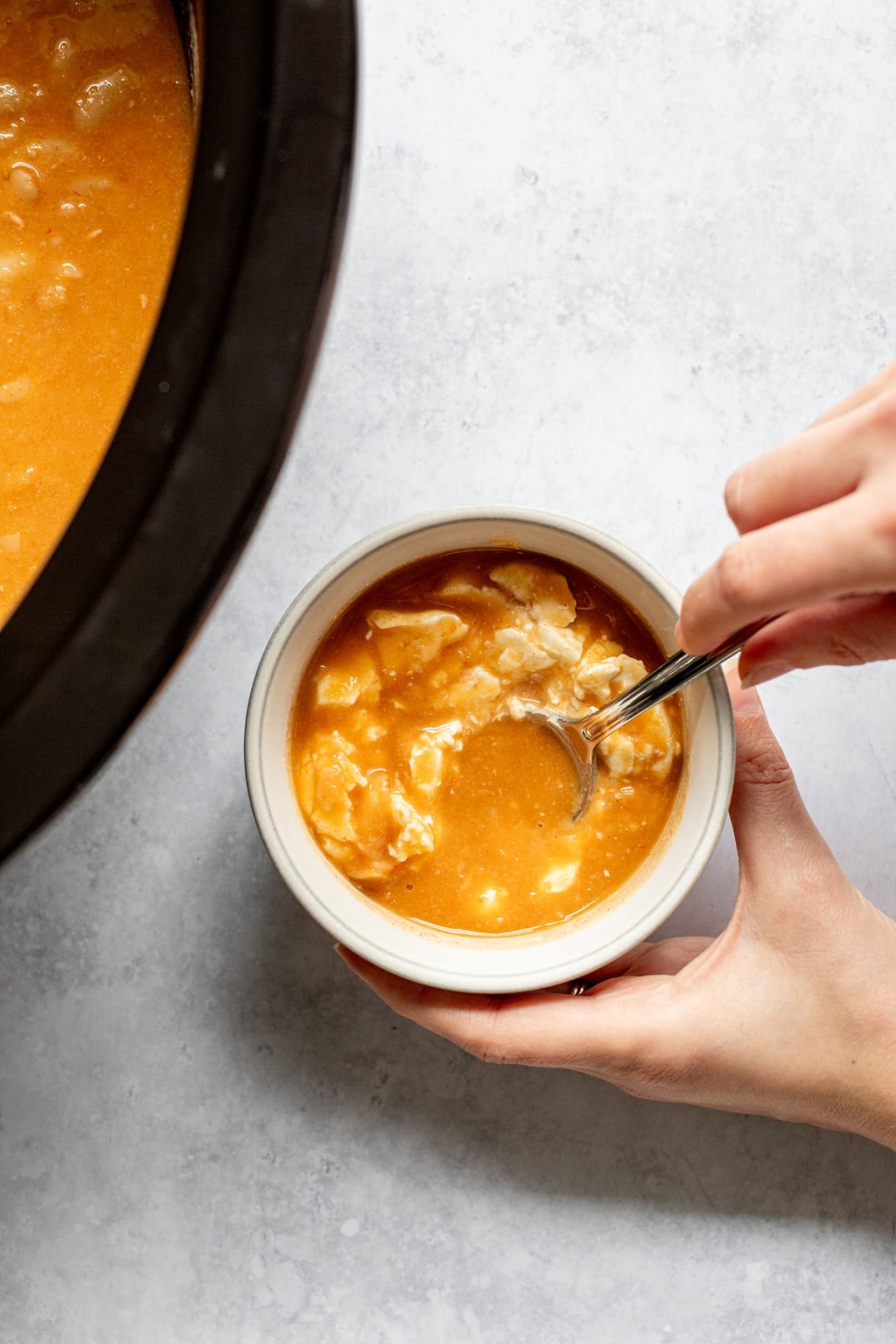 Overhead shot of mixing cream cheese and buffalo chicken chili broth in a small white bowl.
