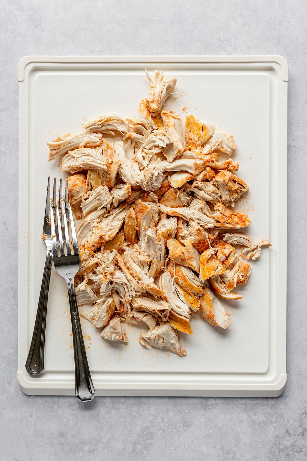 Overhead shot of white cutting board with two forks and shredded buffalo chicken.