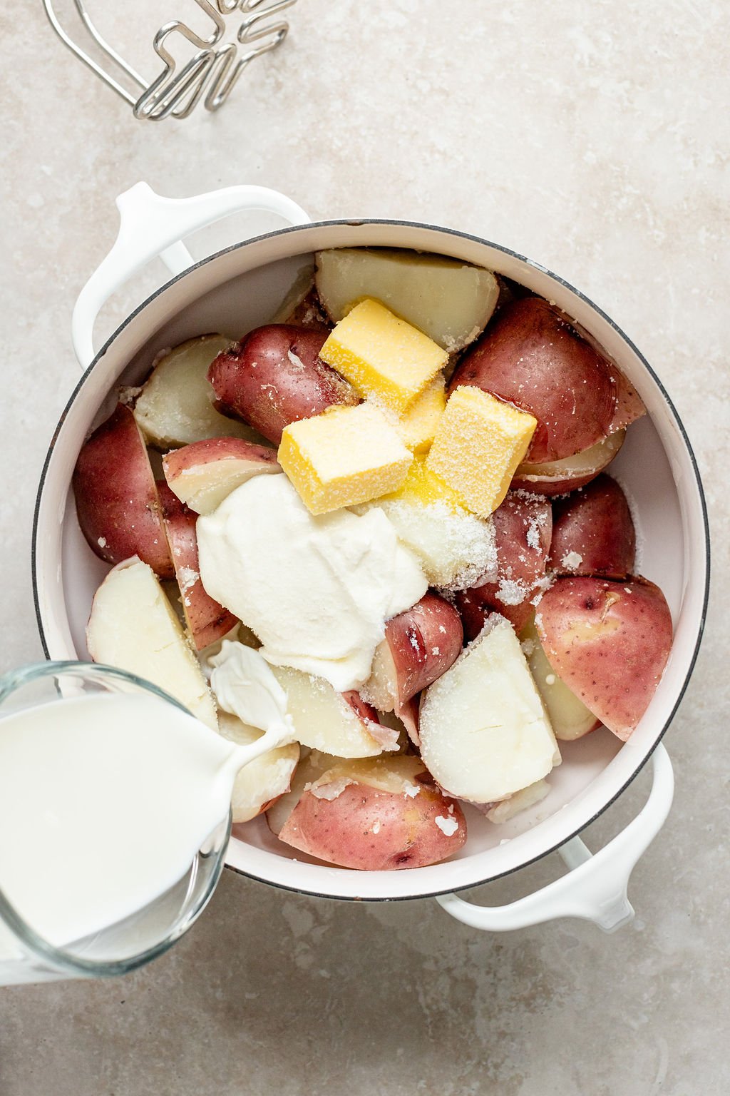 Overhead image of milk being poured into a pot with cooked potatoes, sour cream, butter, and salt.