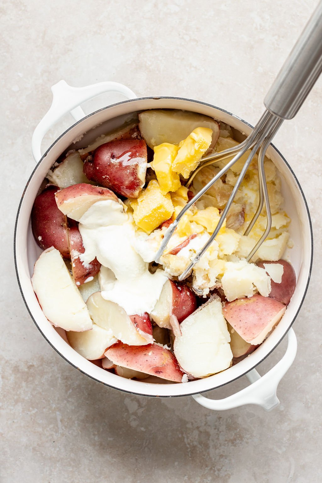 Overhead image of mashing cooked potatoes, sour cream, butter, and salt.